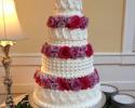 A 4 tier wedding cake with various designs on each tier as well as purple and pink flowers.
