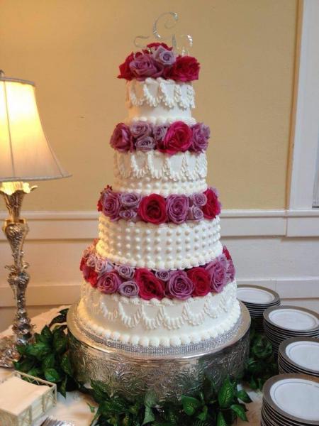 A 4 tier wedding cake with various designs on each tier as well as purple and pink flowers.